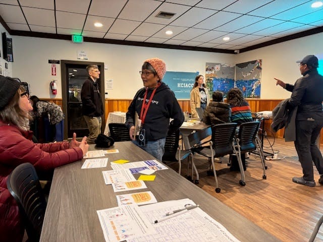 Organisator*innen bei einer Veranstaltung zum Thema Community Organizing. Das Foto zeigt einen Saal, in dem Menschen stehen und an Tischen sitzen und sich unterhalten.